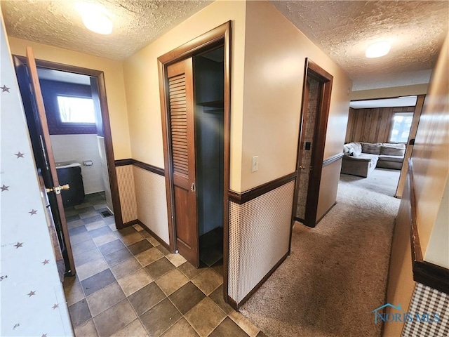 corridor featuring a textured ceiling, dark carpet, and wainscoting