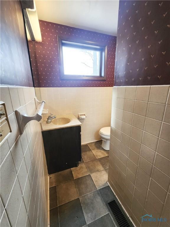 3221 Carrell Rd, Bucyrus, OH 44820 - bathroom with wallpapered walls, tile walls, toilet, a wainscoted wall, and vanity