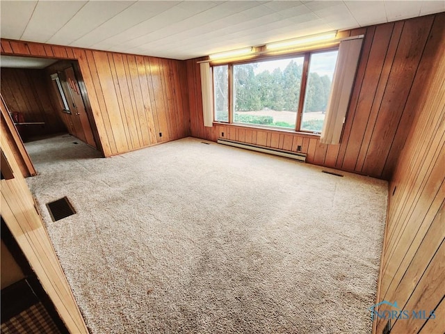 unfurnished room with wood walls, baseboard heating, carpet, and visible vents