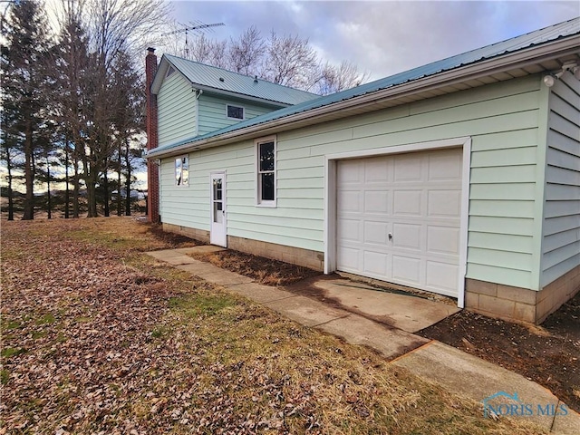 view of side of home featuring a garage, metal roof, and a chimney