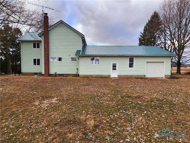 rear view of property featuring an attached garage, a chimney, and metal roof