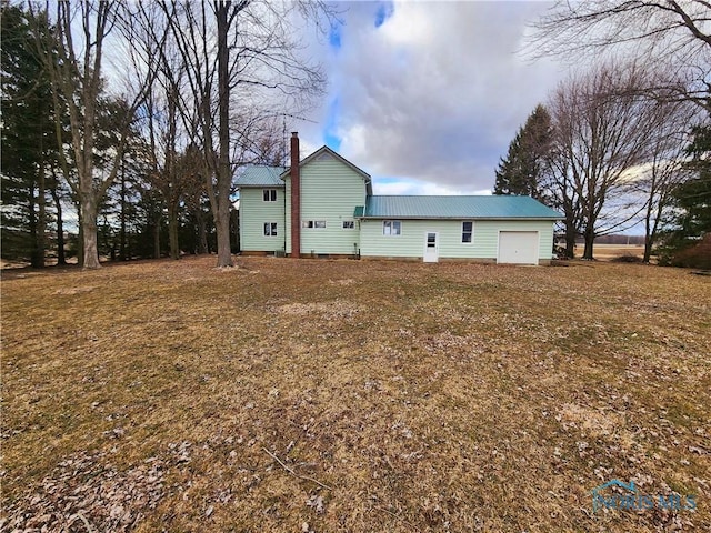 back of house with metal roof, a chimney, and an attached garage