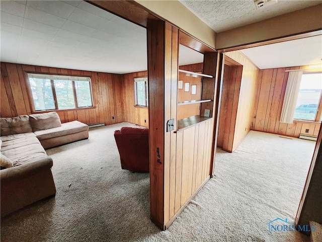 living area featuring a wealth of natural light, carpet, wooden walls, and a baseboard radiator