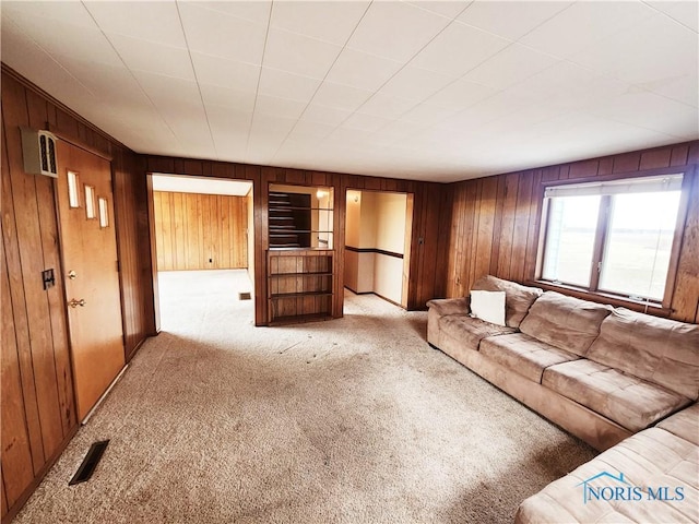 unfurnished living room featuring carpet flooring, visible vents, and wooden walls