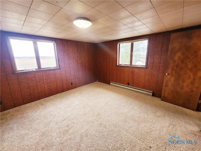 carpeted spare room featuring baseboard heating and wooden walls