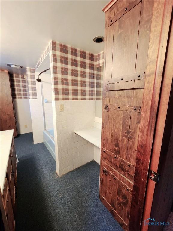 bathroom featuring a bathing tub, a wainscoted wall, tile walls, a shower, and wallpapered walls