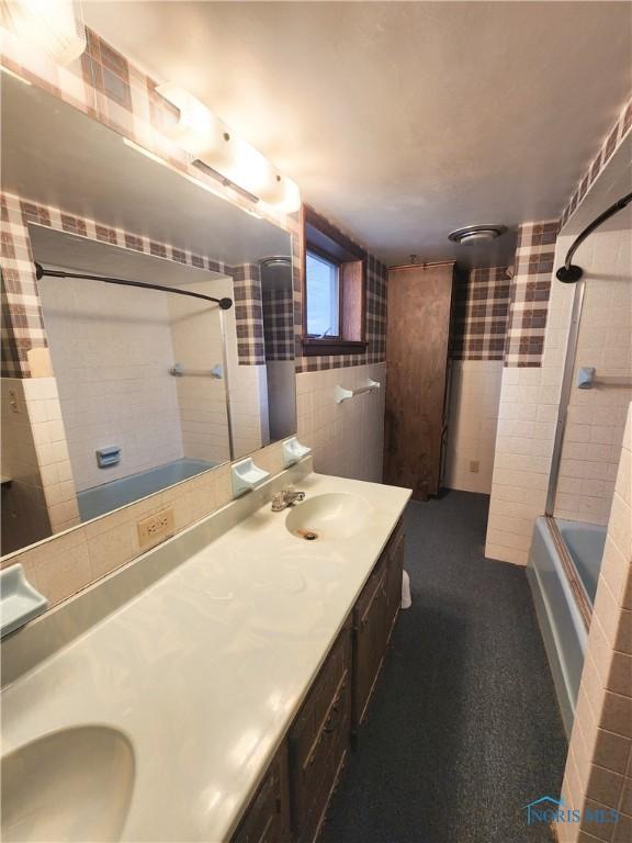 bathroom featuring  shower combination, double vanity, tile walls, and a sink