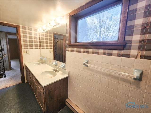 full bath with wainscoting, a sink, tile walls, and wallpapered walls