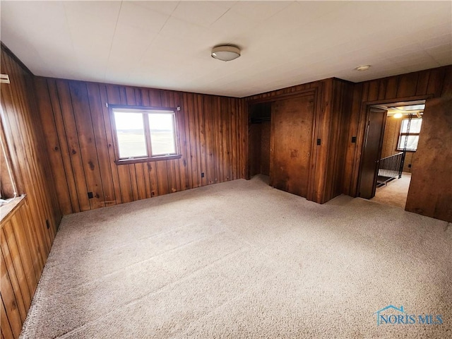 empty room featuring a wealth of natural light, light carpet, and wooden walls