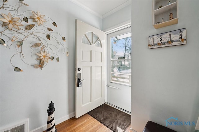 foyer entrance with ornamental molding, light wood-type flooring, visible vents, and baseboards