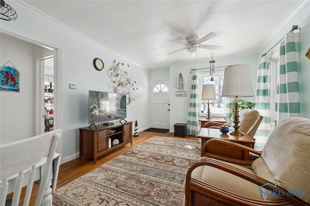 living area featuring a ceiling fan, crown molding, baseboards, and wood finished floors