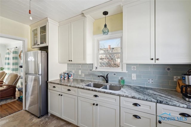 kitchen featuring light stone counters, a sink, white cabinets, backsplash, and freestanding refrigerator