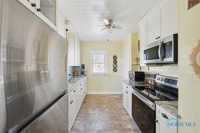 kitchen with light stone counters, stainless steel appliances, backsplash, white cabinets, and baseboards