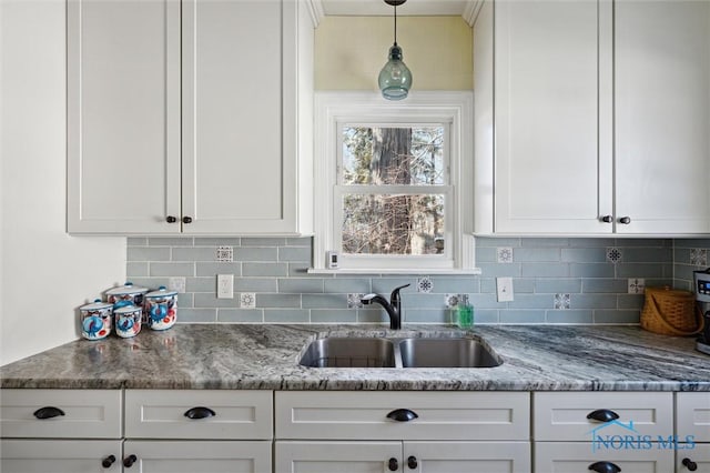 kitchen with pendant lighting, tasteful backsplash, white cabinets, a sink, and light stone countertops