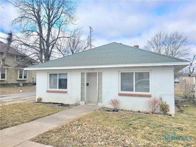 bungalow featuring roof with shingles, a front yard, and stucco siding