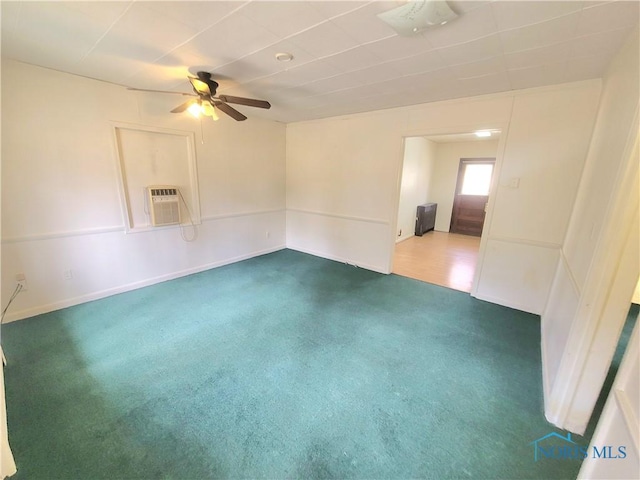 spare room featuring dark carpet, a wall unit AC, a ceiling fan, and baseboards