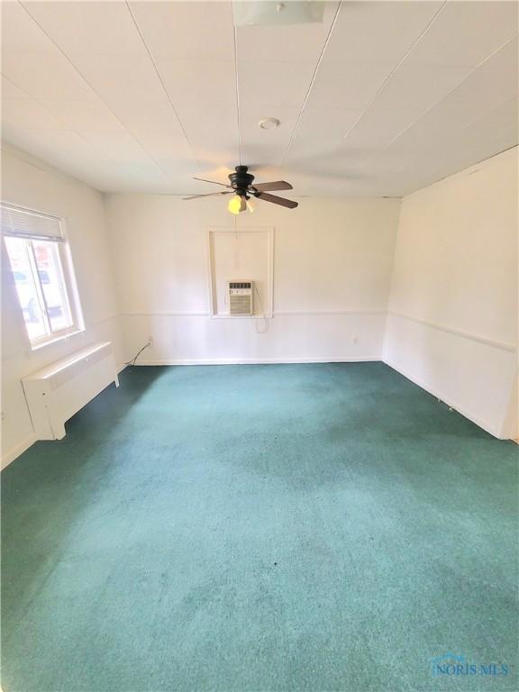 unfurnished room featuring a ceiling fan, a wall mounted air conditioner, carpet flooring, and radiator heating unit