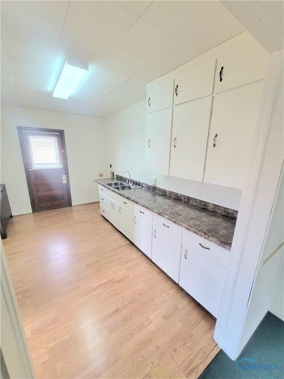 kitchen featuring dark countertops, light wood-type flooring, a sink, and white cabinetry