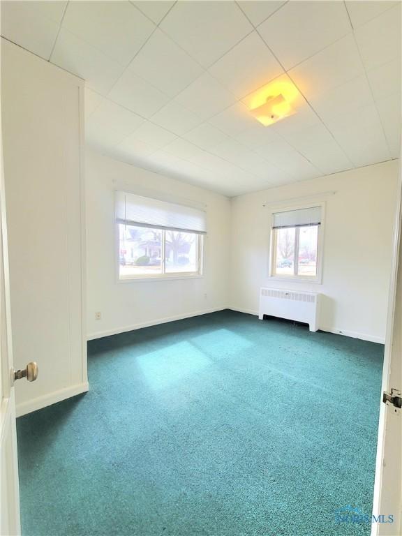 spare room featuring baseboards, radiator heating unit, carpet flooring, and a healthy amount of sunlight