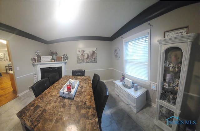 dining area with vaulted ceiling, tile patterned flooring, a glass covered fireplace, and baseboards