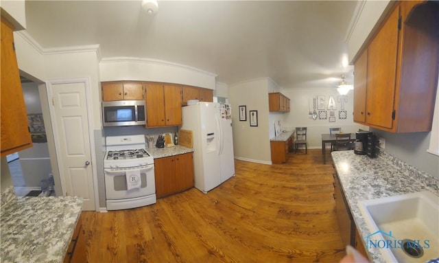 kitchen with appliances with stainless steel finishes, brown cabinets, wood finished floors, ornamental molding, and a sink