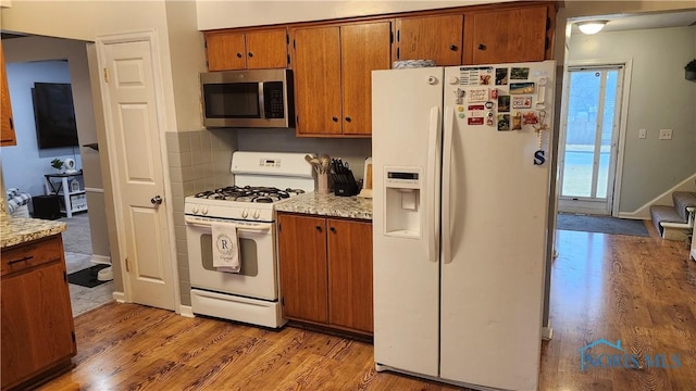 kitchen with white appliances, light countertops, light wood-type flooring, brown cabinets, and tasteful backsplash