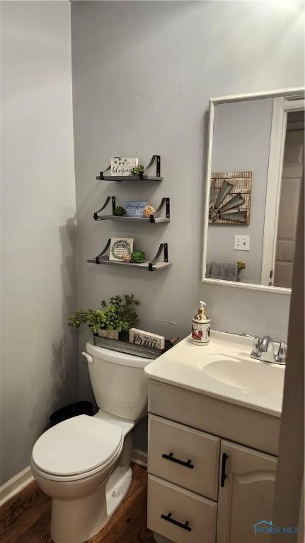 half bath featuring toilet, wood finished floors, and vanity