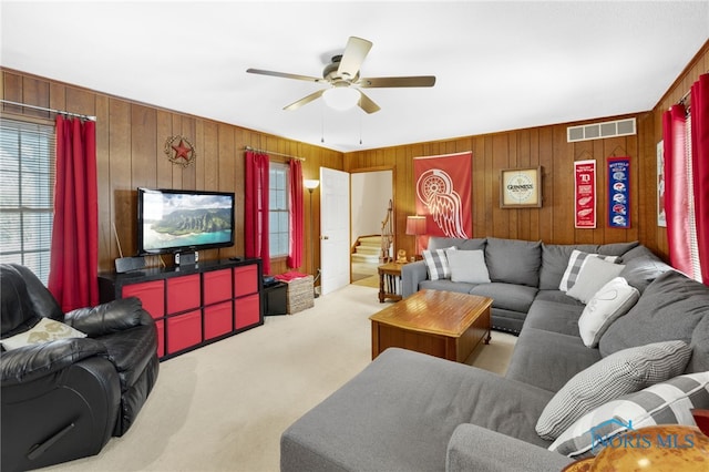 living room featuring carpet, visible vents, stairway, a ceiling fan, and wooden walls