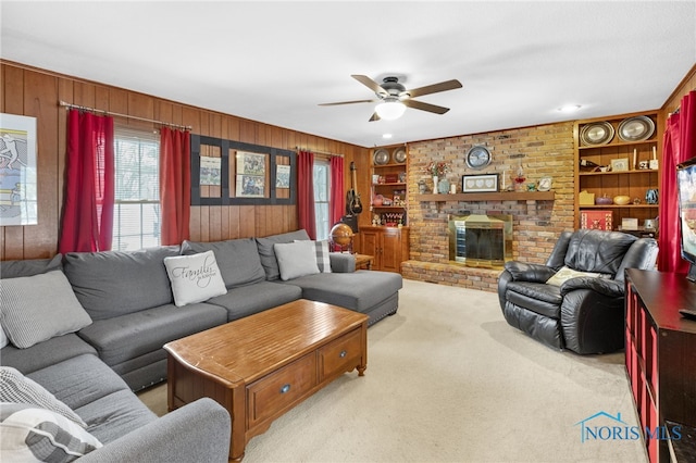 living area featuring light carpet, wooden walls, built in features, a ceiling fan, and a brick fireplace