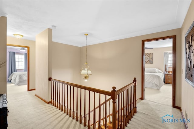 hallway featuring baseboards, light colored carpet, and an upstairs landing