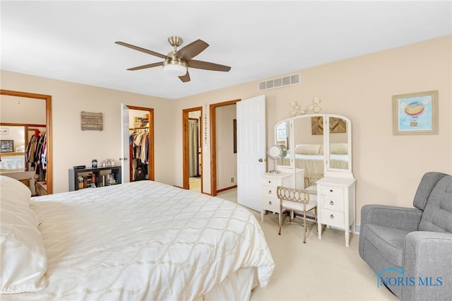 bedroom with a ceiling fan, a walk in closet, visible vents, and light carpet