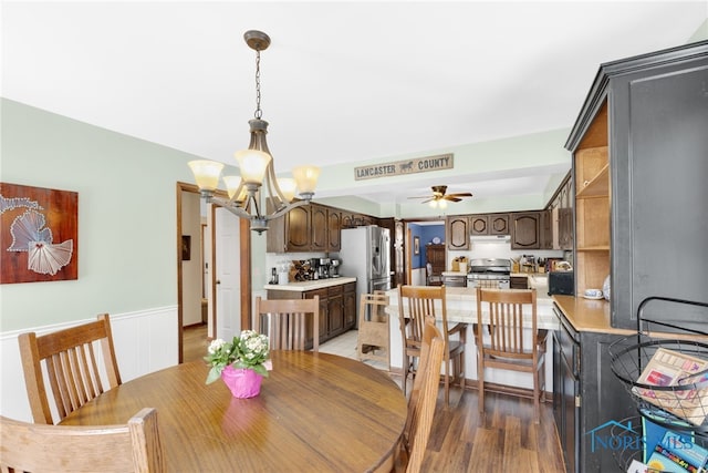 dining area featuring light wood-style floors, ceiling fan with notable chandelier, and wainscoting