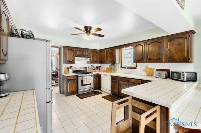 kitchen with under cabinet range hood, a sink, dark brown cabinets, appliances with stainless steel finishes, and tile counters