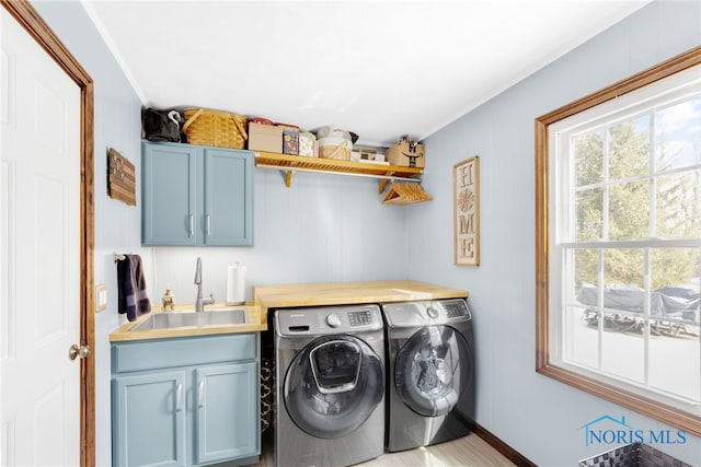 clothes washing area featuring baseboards, a sink, cabinet space, and washer and dryer