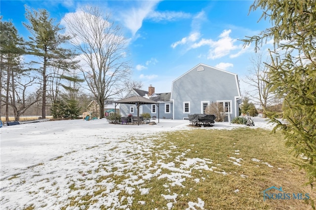 snow covered house featuring a gazebo, outdoor dining area, and a chimney