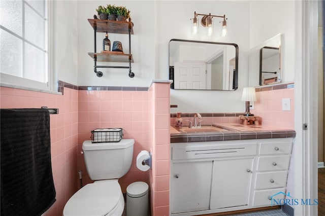 bathroom with wainscoting, toilet, tile walls, and vanity