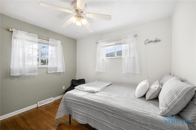 bedroom with baseboards, multiple windows, visible vents, and wood finished floors