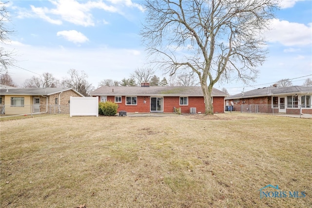 view of front facade featuring brick siding, a chimney, a front yard, and fence