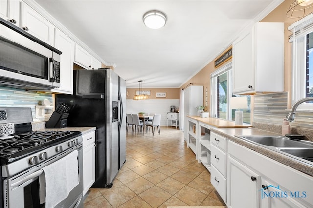 kitchen with stainless steel appliances, a sink, white cabinets, backsplash, and crown molding