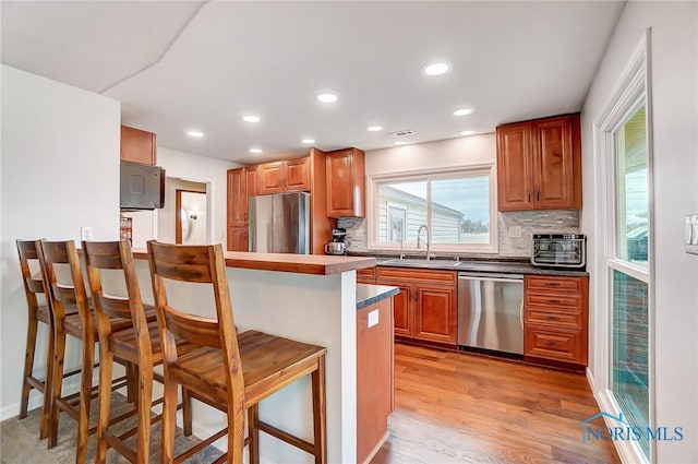 kitchen with a breakfast bar, light wood finished floors, tasteful backsplash, appliances with stainless steel finishes, and a sink