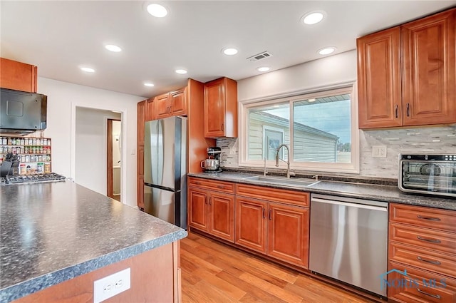 kitchen with a sink, visible vents, appliances with stainless steel finishes, light wood finished floors, and dark countertops