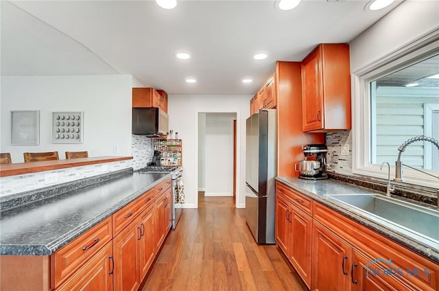 kitchen with light wood finished floors, dark countertops, stainless steel appliances, a sink, and recessed lighting