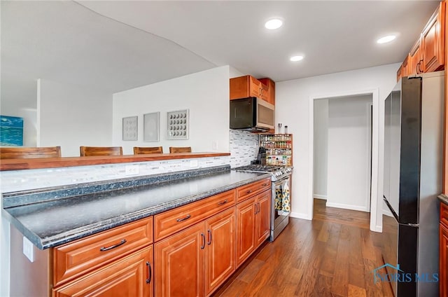 kitchen with dark wood finished floors, brown cabinets, stainless steel appliances, backsplash, and recessed lighting