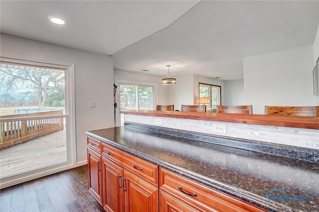 kitchen featuring pendant lighting, recessed lighting, dark wood-type flooring, brown cabinetry, and dark stone countertops