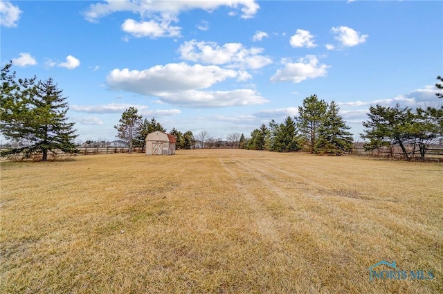 view of yard with an outbuilding, a rural view, fence, and a storage shed