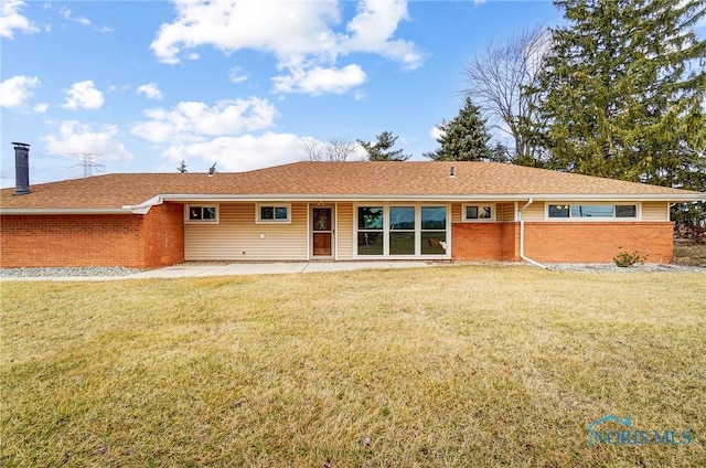 view of front facade with roof with shingles, a front yard, a chimney, and brick siding