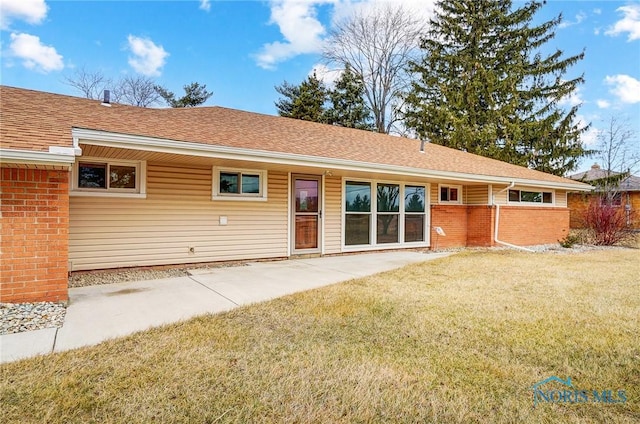 rear view of property featuring roof with shingles, a lawn, and brick siding