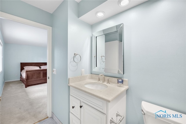 half bath featuring baseboards, vanity, toilet, and ensuite bathroom