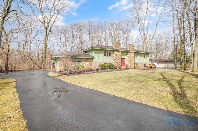 view of front of home with a garage, driveway, stone siding, a chimney, and a front yard