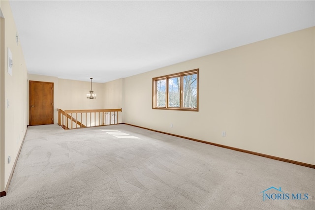 carpeted spare room featuring an inviting chandelier and baseboards